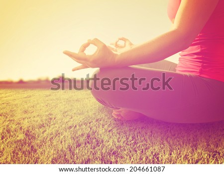 hands of a woman meditating in a yoga pose on the grass toned with a soft instagram like filter
