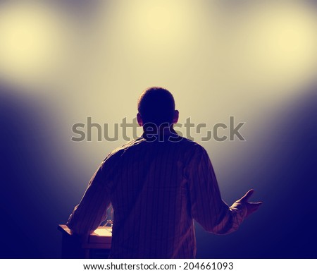 a young man in front of a podium and an audience a young man in front of a podium and an audience