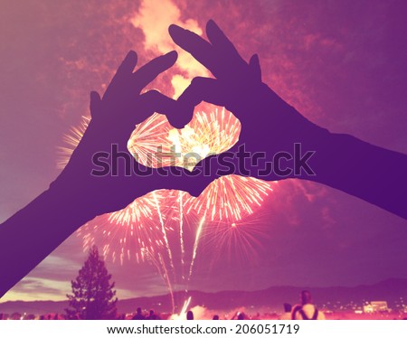 a silhouette of hands shaped in a heart against a 4th of july fireworks background