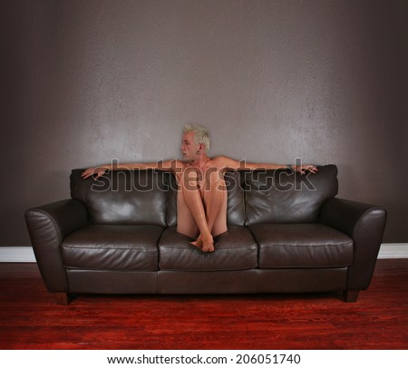 a young male sitting down on a brown leather couch