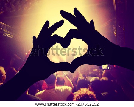 a crowd of people at a concert  with a heart silhouette on the singer toned with a vintage retro instagram filter