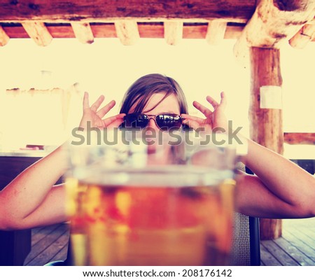 woman peeking over a fresh draft beer as her drink toned with a vintage retro style instagram filter