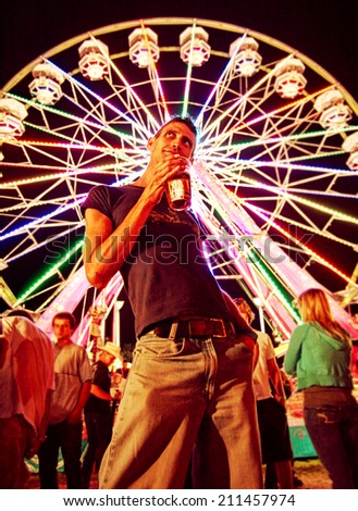 a young man making a funny face at a local state fair at night toned with a retro vintage instagram filter