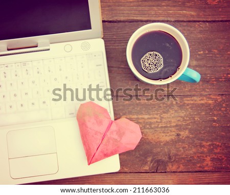 Laptop or notebook with cup of coffee and origami heart on old wooden table toned with a retro vintage instagram filter