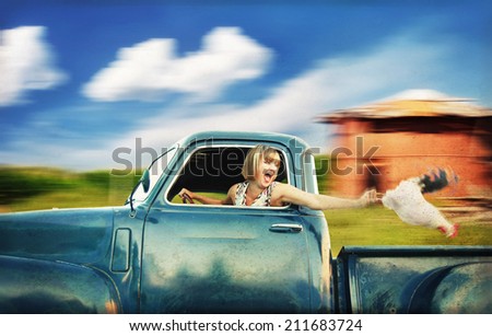 a pretty woman driving a truck past a red barn next to a cornfield