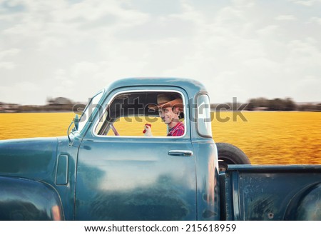 a handsome man with a cowboy hat on driving a truck past a field full of yellow flowers