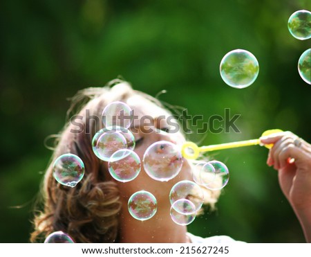 a beautiful woman blowing bubbles outside in a park or backyard on a warm sunny summer day