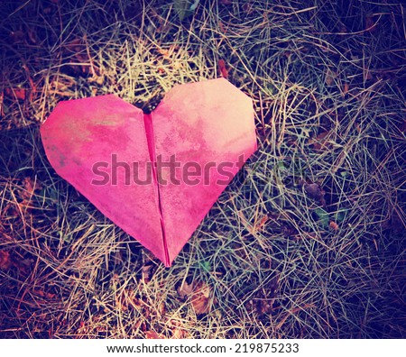an origami heart on grass with sun spots shining on it toned with a retro vintage instagram filter (shallow depth of field)