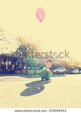 a cute boy playing with a balloon in a city setting toned with a retro vintage instagram filter