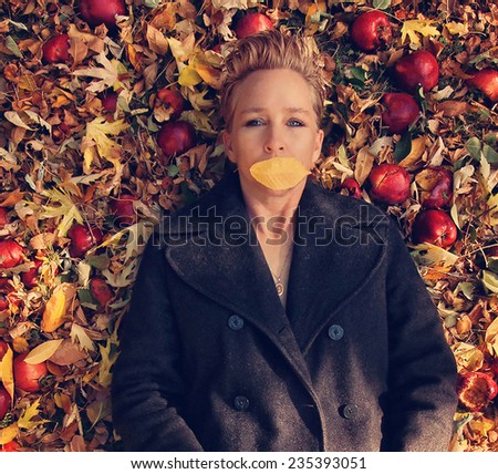 a woman in a nice jacket with a a leaf over her mouth laying in a pile of leaves and apples toned with a retro vintage instagram like filter effect