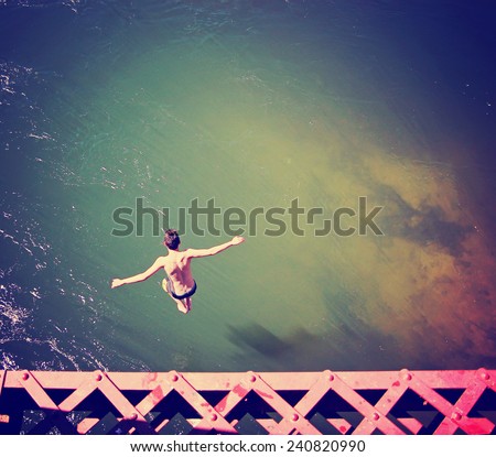 a boy jumping of an old train trestle bridge into a river toned with a retro vintage instagram filter effect