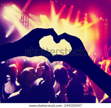a crowd of people at a concert with heart shaped hands over the stage toned with a retro vintage instagram filter