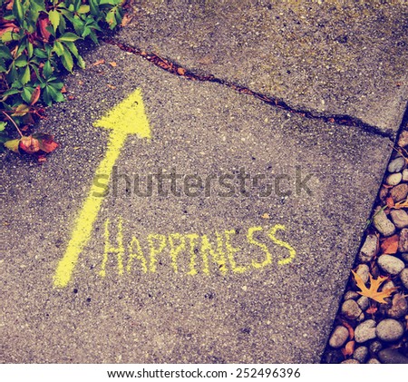a yellow arrow showing the way to happiness written on a sidewalk with chalk toned with a retro vintage instagram filter effect (very shallow depth of field)