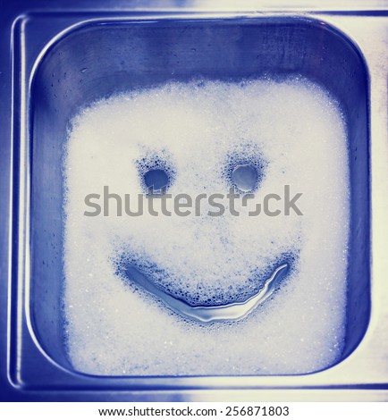 Detergent or soap bubbles and water in the shape of a smiley face in a sink toned with a retro vintage instagram filter effect app or action