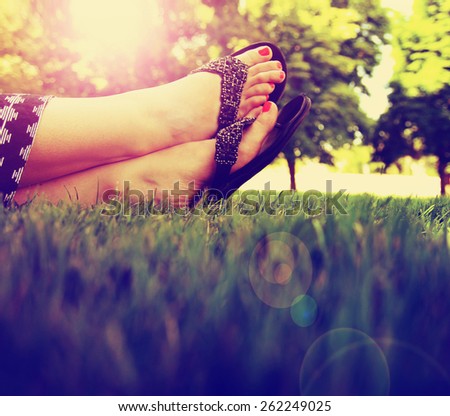 pretty feet on grass at sunset with nails painted and sandals on toned with a retro vintage instagram filter