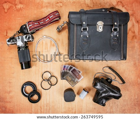 overhead image of old dirty scratched up gear needed for old school film photography enthusiasts including two cameras, a case, filters and a shutter release cable