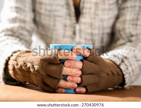 Hot drink in a blue mug in hands with gloves on close up