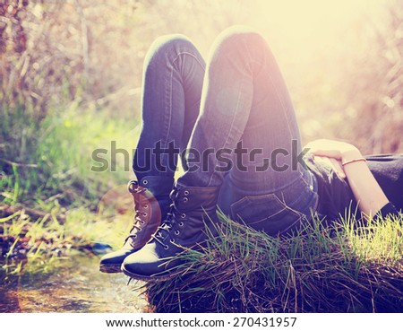 a girl lying on a small island in a stream with jeans and black combat boots on backlit with the setting sun toned with a retro vintage instagram filter effect app or action