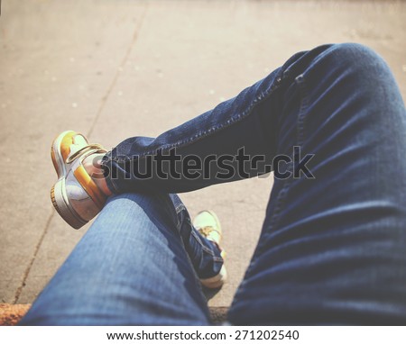 a hipster sitting downtown with crossed legs on a sidewalk bench on a sunny day toned with a retro vintage instagram filter app or action (focus on foot)