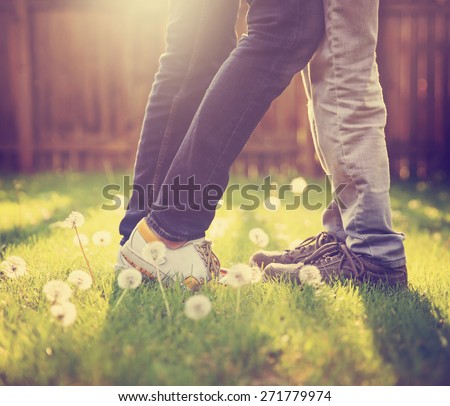 young couple kissing in a backyard in summer sun light at sunset with dandelions blooming toned with a retro vintage instagram filter app or action effect (very shallow depth of field - on the shoes)