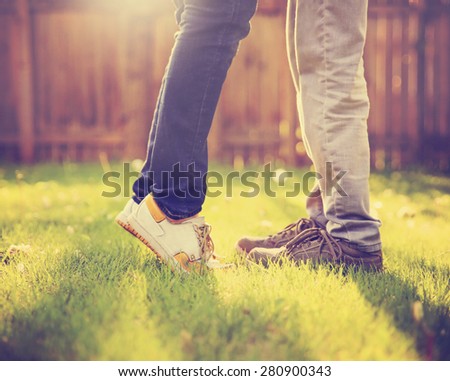 A young couple kissing in a backyard in summer sun light during sunset with dandelions blooming toned with a retro vintage instagram filter (VERY SHALLOW DOF on legs)