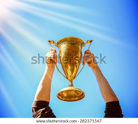 a man holding up a gold trophy cup as a winner in a competition (SHALLOW DOF on trophy) generic text