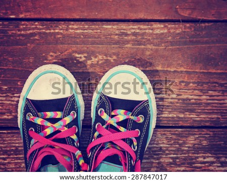 a wide angle photo of a pair of shoes with pink shoe laces on a vintage wooden background toned with a retro vintage instagram filter app