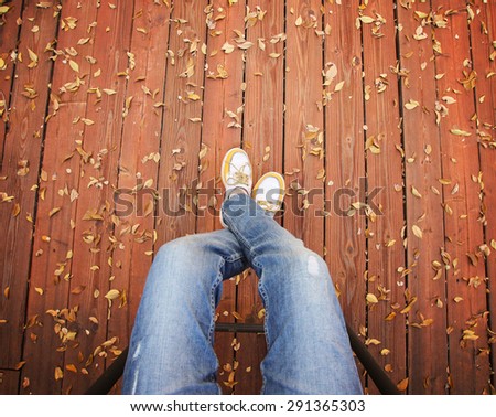 a pair of legs taken from overhead on a deck with leaves that have fallen