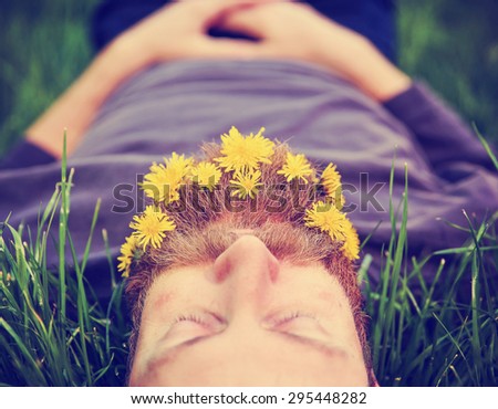 a sleeping hipster lying in tall grass with dandelions in his epic beard taking a nap toned with a retro vintage instagram filter and light leaks