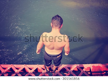a boy getting read to jump off an old train trestle bridge into a river on a hot summer day toned with a retro vintage instagram filter app or action effect