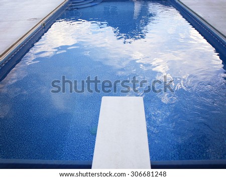 a local public pool without any people in it with a diving board and reflections of clouds