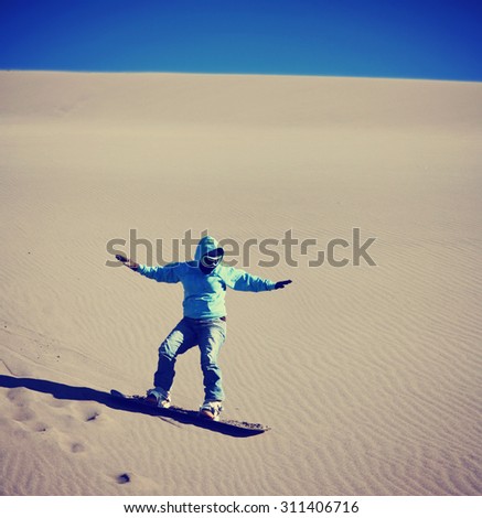 a woman sand boarding down a sandy dune hill with goggles and a sweatshirt hoodie on a snowboard toned with a retro vintage instagram filter effect app or action
