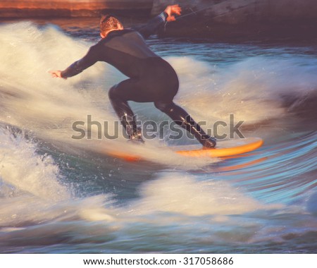 motion blur of a surfer riding a wave in a full wet suit toned with a retro vintage instagram filter app or action effect (SHALLOW DOF action shot)