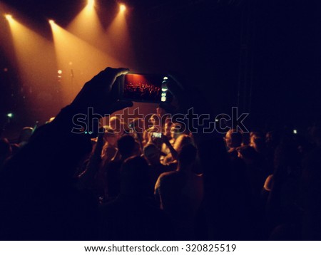 a crowd of people at a concert with one holding a cell phone taking a photo toned with a retro vintage instagram filter effect app or action