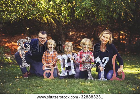a cute family posing with letters made of wood in a park toned with a retro vintage instagram filter effect app or action