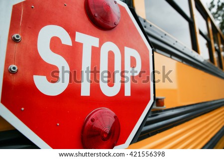 wide angle front view of a bright yellow orange school bus and the big red stop sign