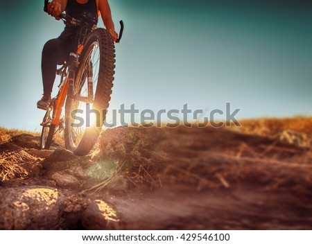 a woman riding a bicycle down a dirt trail with big rocks in the back country to get away from the city toned with a retro vintage instagram filter app or action effect