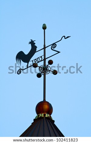 Old weather vane in the form of a cockerel on the roof of a house