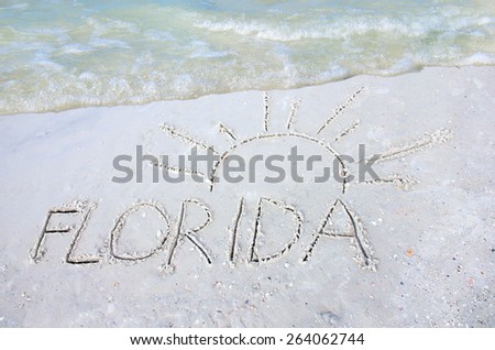 A drawing in the sand at the beach of FLORIDA with a sun over it with a colorful wave coming in from the top representing vacation travel to tropical Florida the sunshine state.