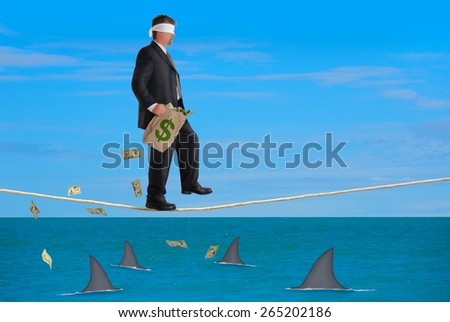 A blindfolded business man with a bag of money is walking a tightrope over a school of sharks representing financial risk, management, success, wise or bad investments and much more in finance.