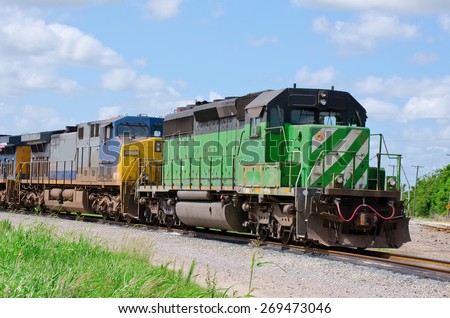 Green freight train pulling a blue and yellow train as they speed down the track