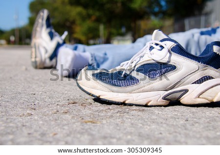 Closeup of the shoe from a pedestrian that is a victim of automobile hit and run on a roadside with the victim laying in the background.