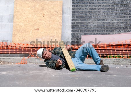 A fallen and injured construction worker in a hard hat laying on the ground at a construction work site