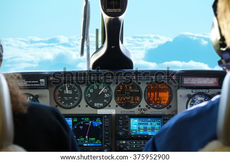 Small twin turbo engine airplane cockpit view while in flight with gauges lit up and fluffy white and blue clouds in the window.