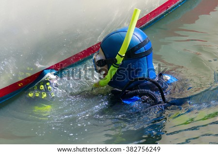 Scuba diver with snorkel and aqualung tank is cleaning a boat hull with a scrubbing pad removing all organic growth so the hull is smooth & clean resulting in higher speeds and better fuel efficiency