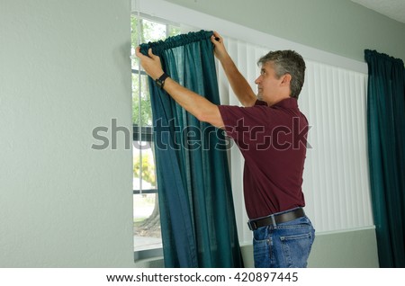A handy man home repair service technician or home owner hanging curtains for the window treatment in a new house.
