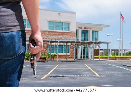 A young man with a pistol gun is standing in front of a high school preparing to commit a crime