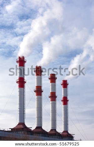 Industrial site with smoking chimneys, steam against blue sky with clouds.
