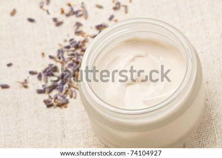 Closeup of open container of moisturizing face cream on a linen and lavender buds around