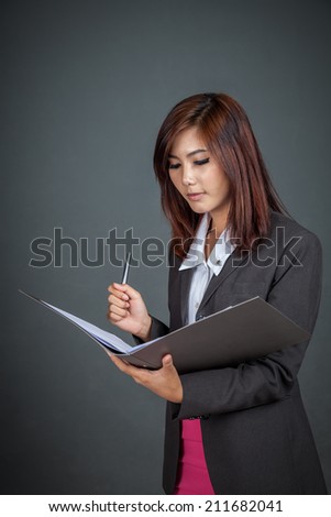 Asian businesswoman with a pen and folder on gray background